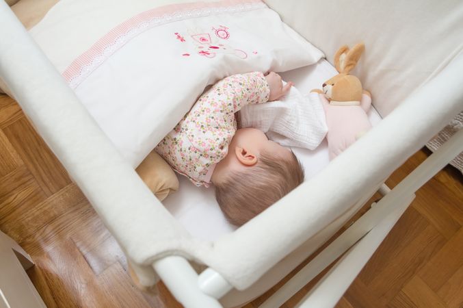 Baby sleeping in a cot with pacifier and toy