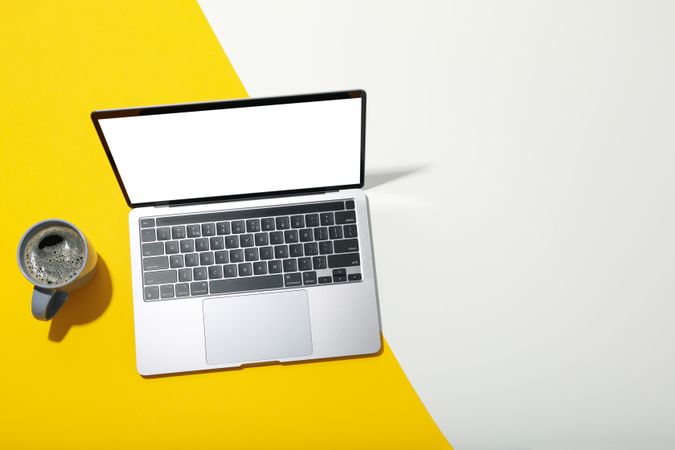 Laptop with mockup screen with mug of coffee on dual tone yellow background with copy space