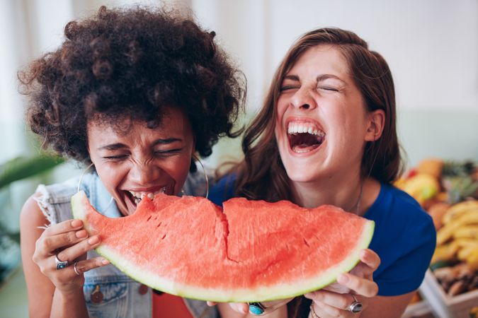 Two female friends laughing hysterically while holding fruit
