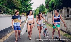 Fun young friends walking along road in summer day with surfboard and bicycle bE99Gl