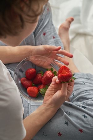 Crop kid eating strawberries from bowl at home