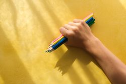 A child's hand picking up coloured pencils on a yellow backgroun