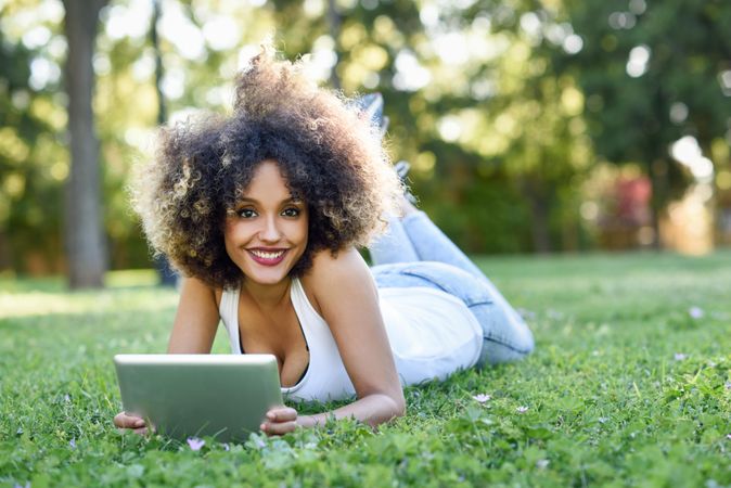 Smiling Black woman with afro hairstyle using digital tablet in park