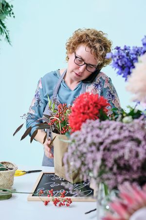 Woman arranging bouquet during phone call in flower store