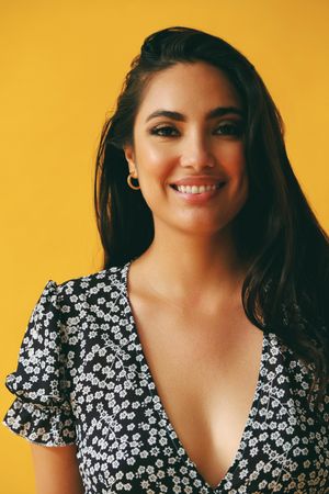 Smiling Hispanic woman wearing dress standing in yellow room, vertical