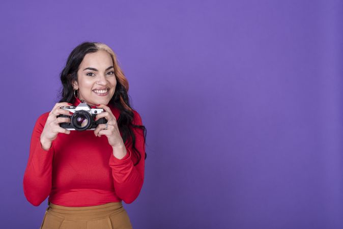 woman taking a photo with her film camera over a violet background. Copy space.