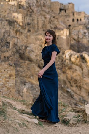Woman in long blue dress standing near abandoned village in Hamsutl, Dagestan