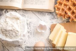 Top view of table with wheat flour, butter, eggs, a cookbook and freshly baked Belgian waffles 5n1w20