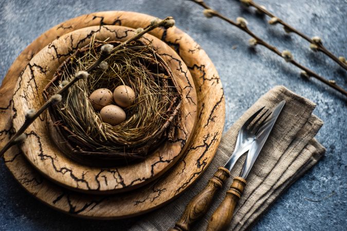 Decorative eggs in delicate nest on rustic brown plate on table