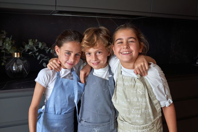 Delightful kids in aprons in dark kitchen