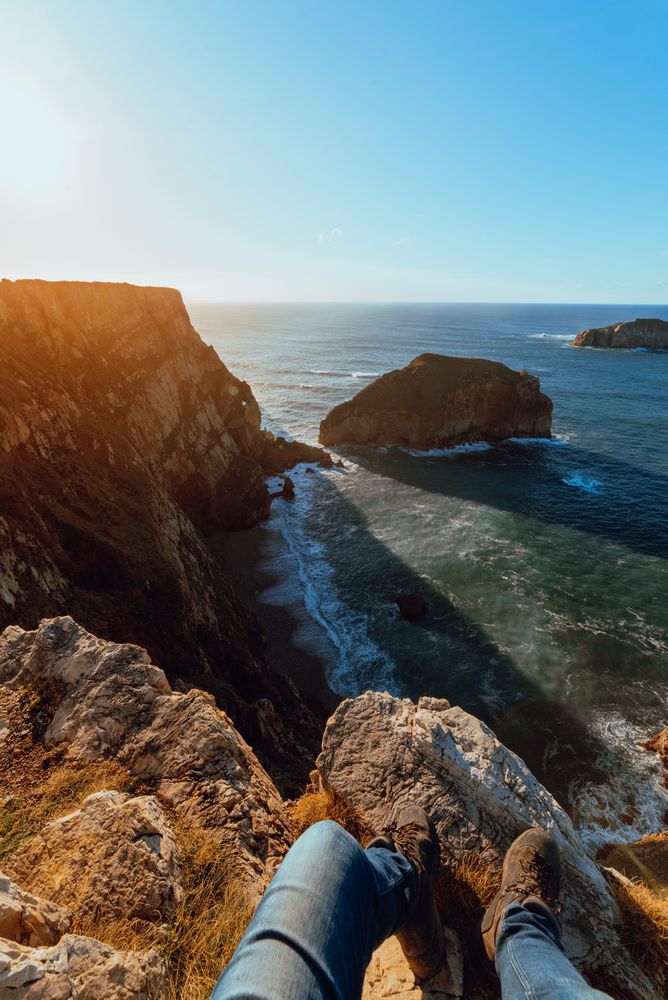 Person sitting on cliff near water