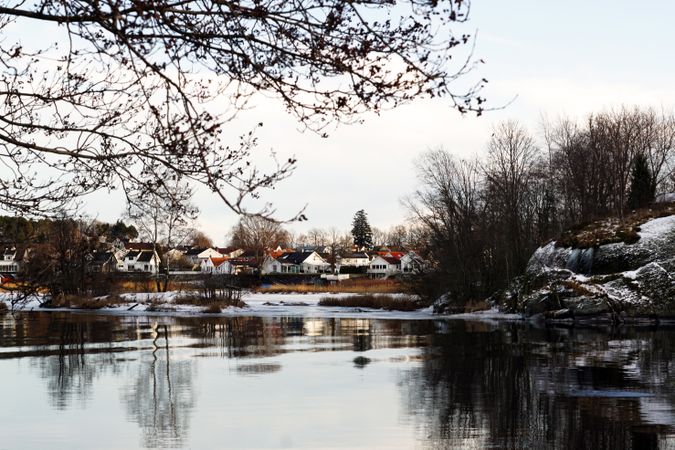 Town at snowy river side and bare trees reflecting in still water