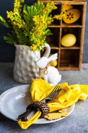 Easter table setting on concrete table with vase of flowers and yellow napkin