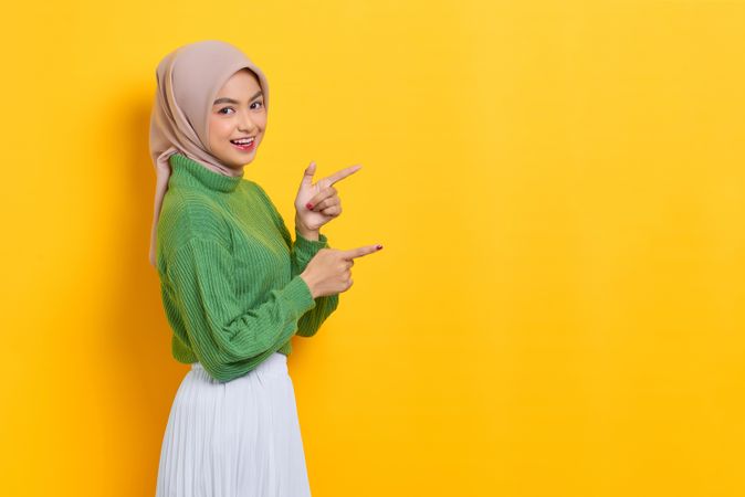 Woman in headscarf standing to the side and pointing at yellow copy space