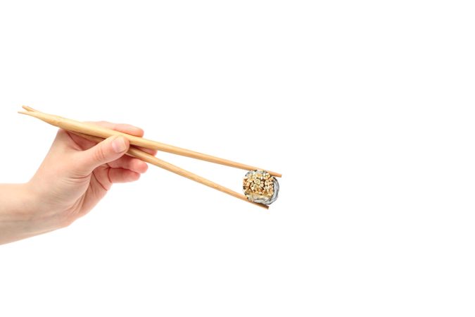 Female hand with chopsticks holds sushi roll, isolated on plain background