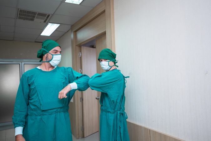 Two medical professionals in scrubs greeting each other with elbow bump in hallway
