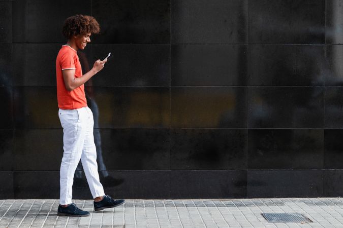 Delighted young guy using smartphone and smiling on street