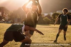 Rugby players running with ball and tackling during game with sun behind 4AOP60