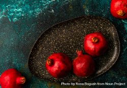 Whole pomegranates on dark ceramic plate on green surface bGjWY4