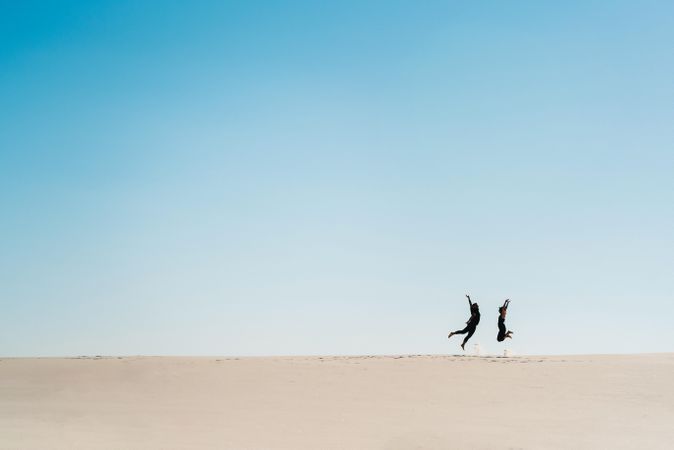Man and woman jumping on sand  under blue sky