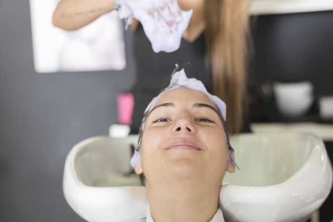 Content female lying back with hairdresser washing her hair