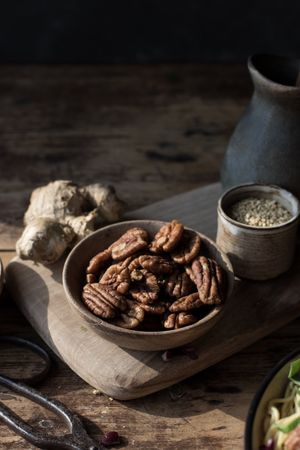 Bowl with pecan nuts near scissors, cutting board, pitcher and ginger