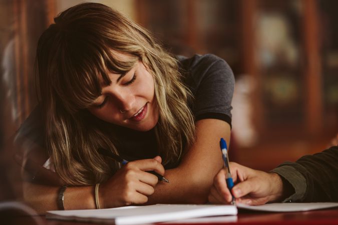 Close up of female student looking at classmate writing in book