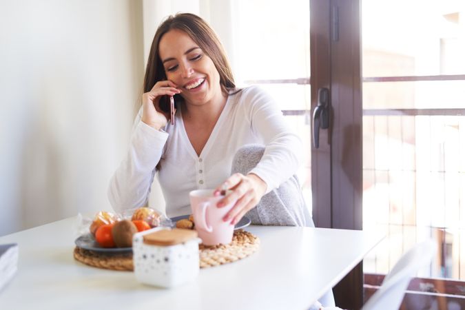 Smiling woman with smartphone eating at table at home
