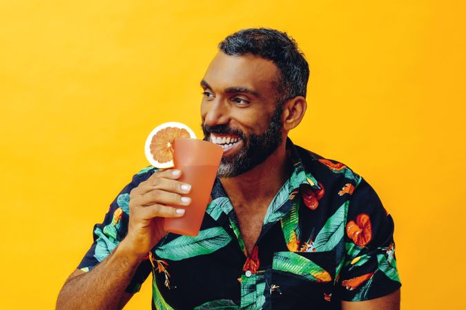 Happy Black male sitting down with cocktail in yellow room