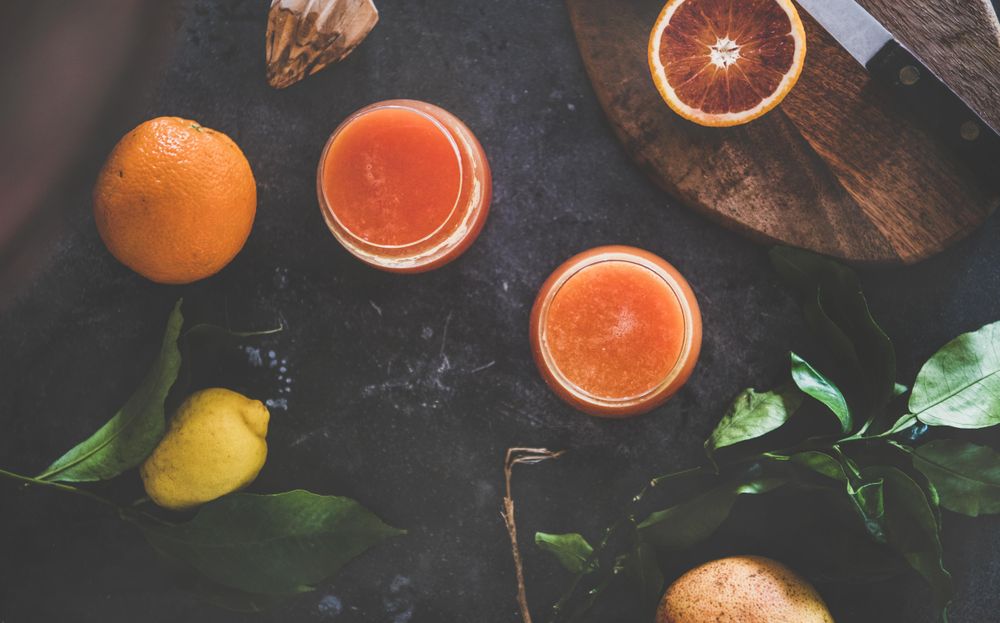Two glasses of freshly squeezed blood orange juice, with squeezer, and fruit, top view