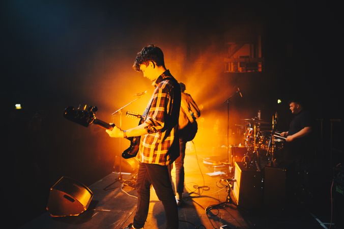 Young white male rock musician  wearing flannel playing bass guitar on stage with orange spotlight