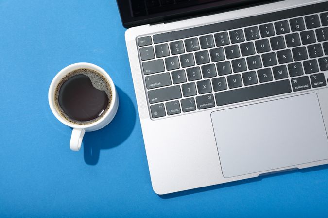 Looking down at blue room with laptop keyboard with cup of coffee