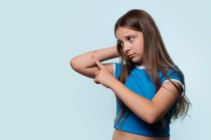 Girl looking worried as she points to cut on elbow