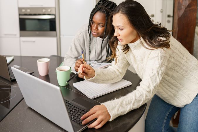 Two women sitting at kitchen table concentrating on their work on a laptop