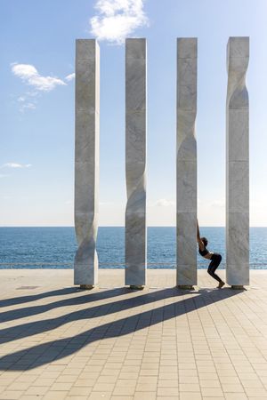 Side view of female stretching on sculpture by the ocean