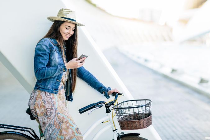 Woman in blue denim jacket riding on bicycle and holding her phone