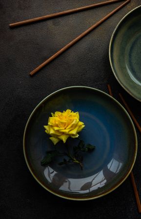 Dark blue table setting with single yellow rose and chopsticks