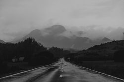 Asphalt road leading between hills to mountain in clouds