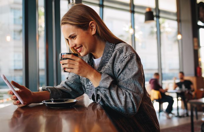 Beautiful woman looking at her phone and drinking coffee at cafe