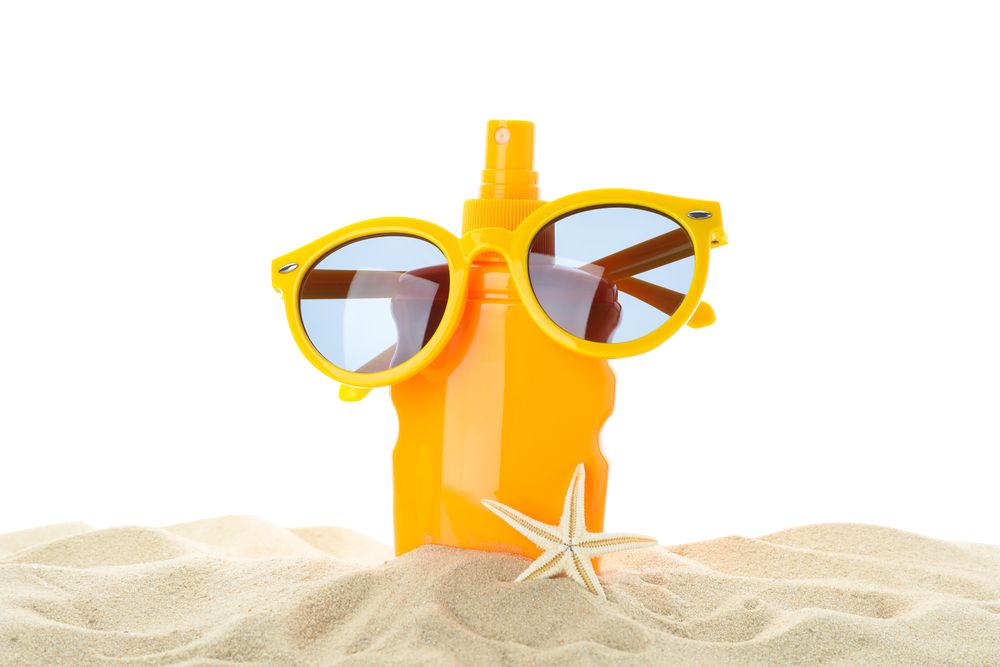 Sunscreen with starfish and sunglasses on clear sea sand isolated on plain background. Summer vacation