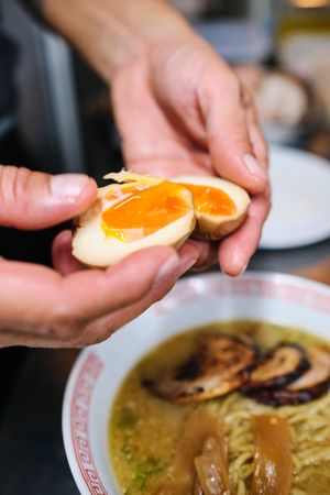Crop person adding boiled eggs to ramen