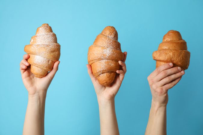 Hands holding croissants on blue background, close up