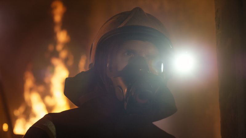 Portrait of a firefighter with mask and fire behind
