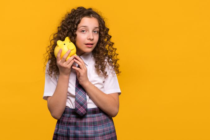 Curious girl listening to yellow piggy bank
