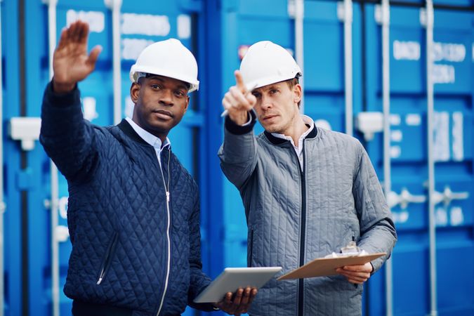Two men in hard hats pointing towards a building project onsite