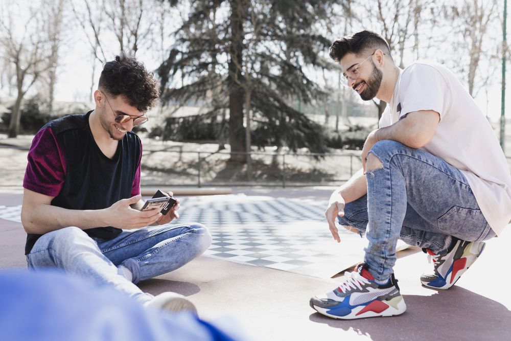 Handsome positive men using smartphone and sitting on floor in park
