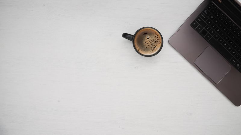 Top view of coffee mug beside laptop on light desk