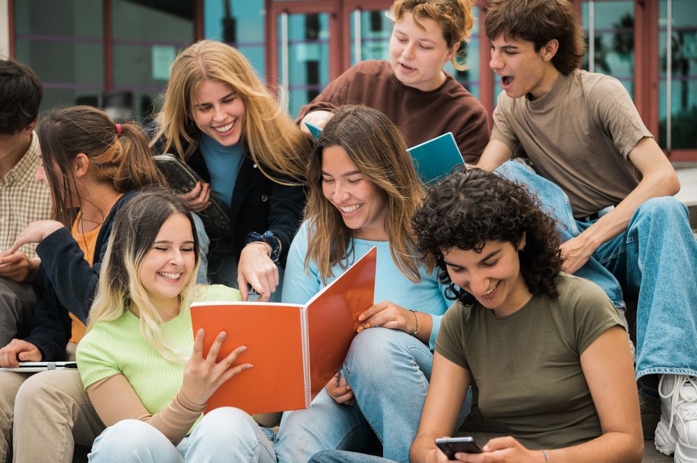 Delighted multiracial students reading notes and smiling on stairs