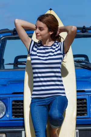 Woman leaning on big surfboard near car