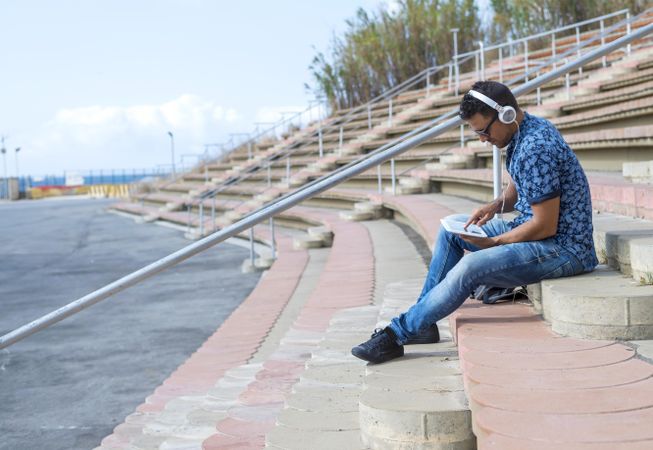 Male sitting on stairs on sunny day and using tablet